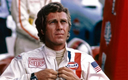 Man in racing suit with Gulf and Heuer patches, adjusting collar at motorsport event