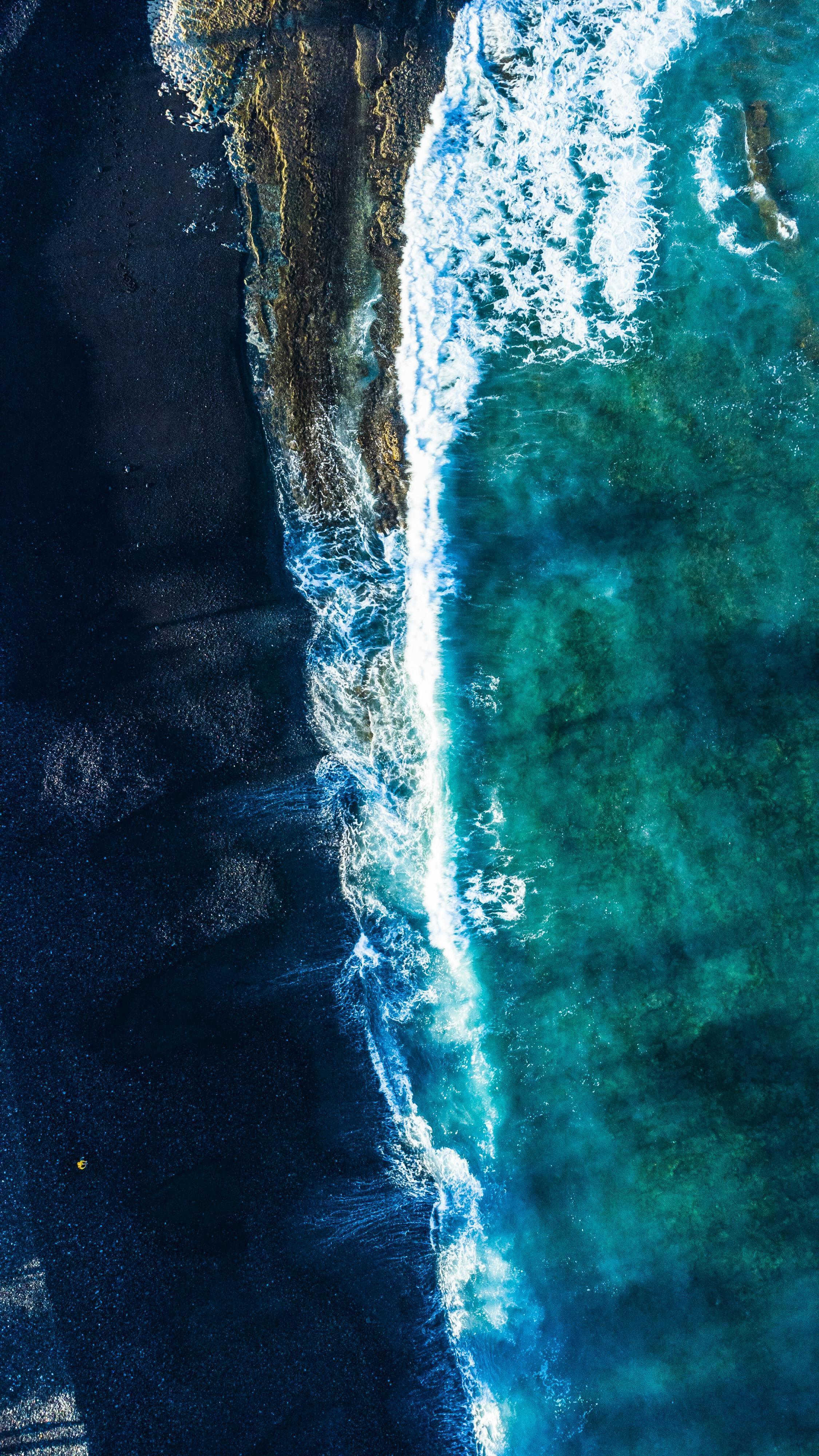 Aerial view of ocean waves crashing onto a dark rocky shoreline